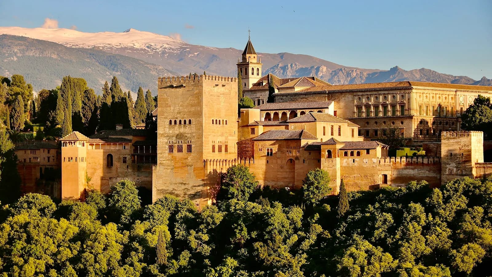 The Alhambra fortress overlooking Granada, surrounded by green trees and Andalusian hillside